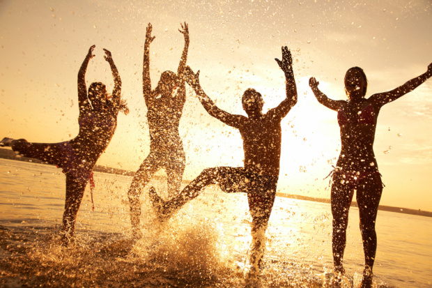 group of happy young people dancing and spraying at the beach on beautiful summer sunset